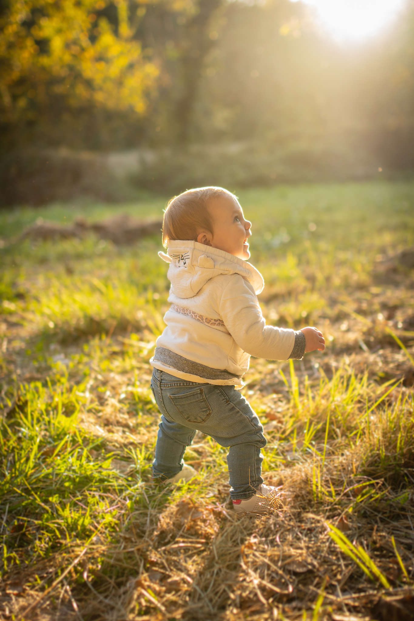 Jeune enfant marchant dans un champ ensoleillé, entouré de nature verdoyante, capturant la douceur d’un moment familial en extérieur. Pour des photos Lifestyle