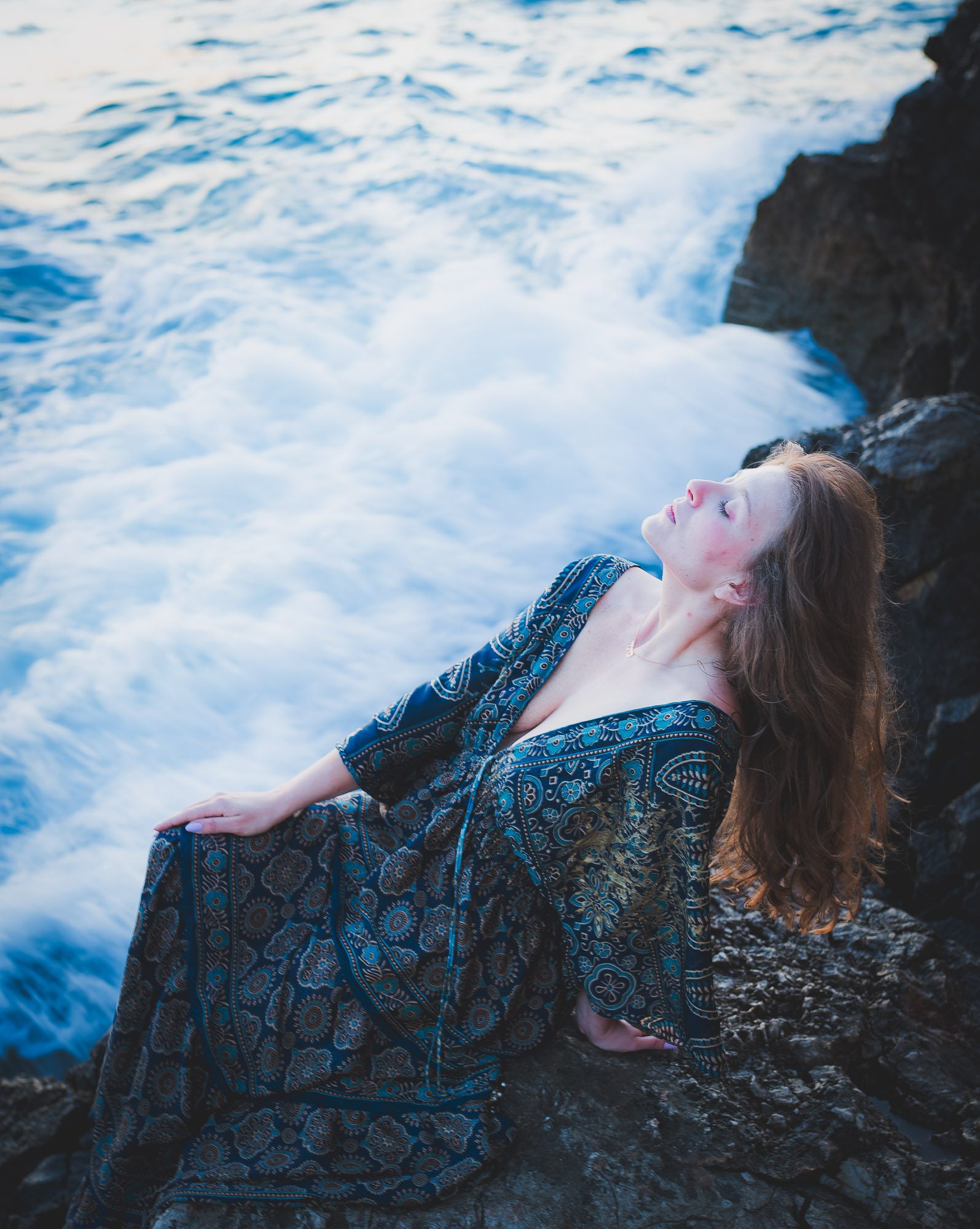 Portrait individuel artistique d’une femme sur les rochers en bord de mer à Nice, robe bleutée.