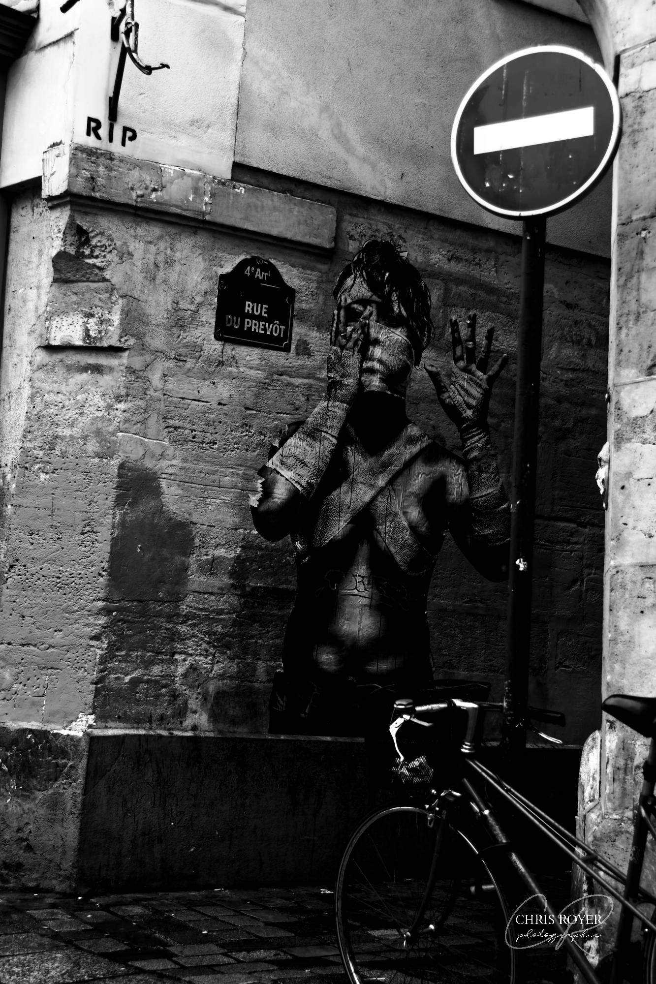 Photo noir et blanc de la rue du Prévôt à Paris avec dessin éphémère sur un mur, vélo et panneau sens interdit