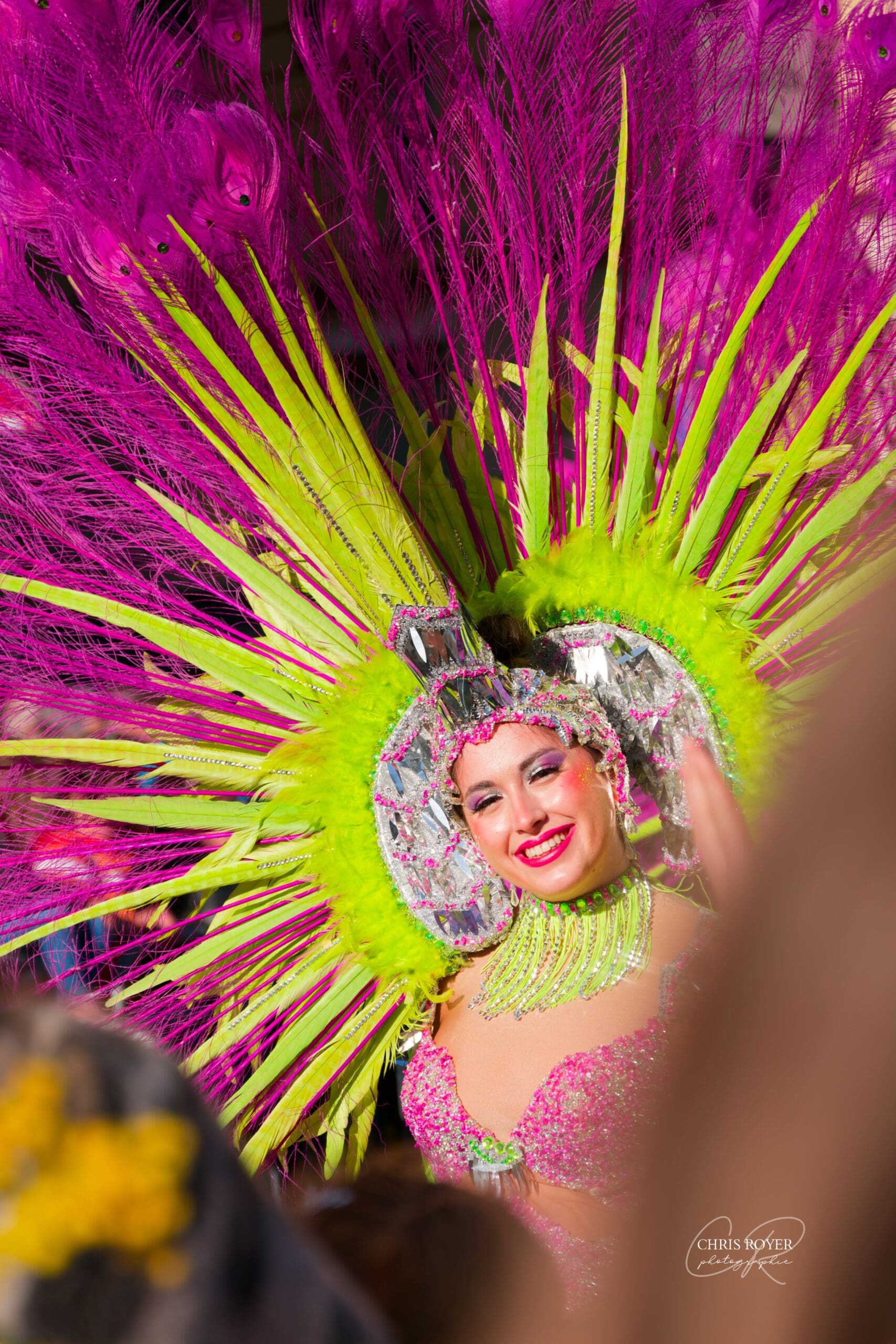 Une artiste portant un costume et une coiffe de plumes colorés sourit lors du défilé du Carnaval Nice 2026