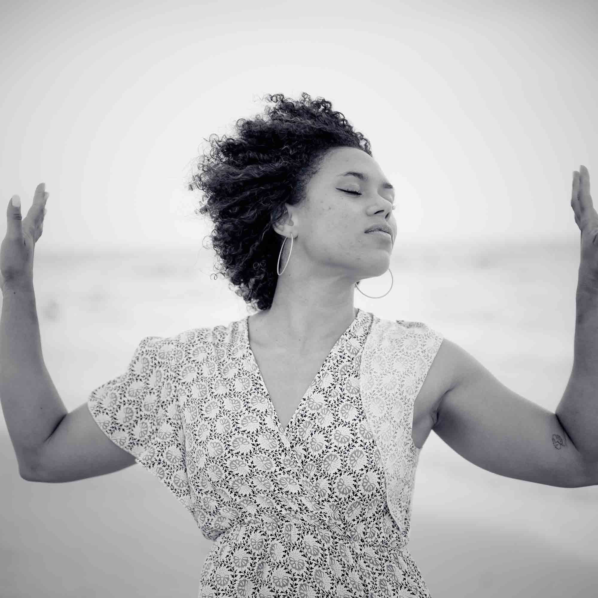 Femme aux cheveux bouclés les yeux fermés bras écartés en bord de mer, portrait noir et blanc par un photographe portrait Nice