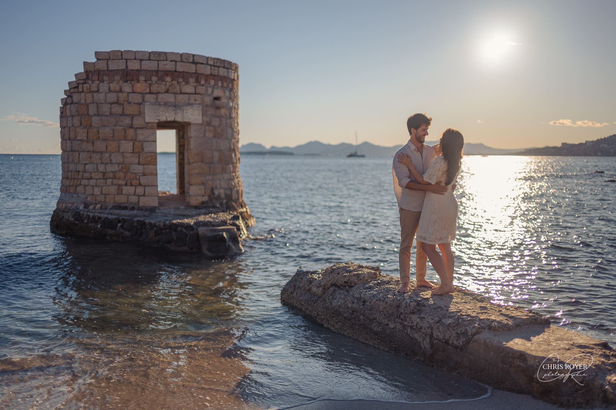Séance photo couple Antibes plage des Ondes - Vue d'ensemble du couple près de la tour historique au coucher du soleil