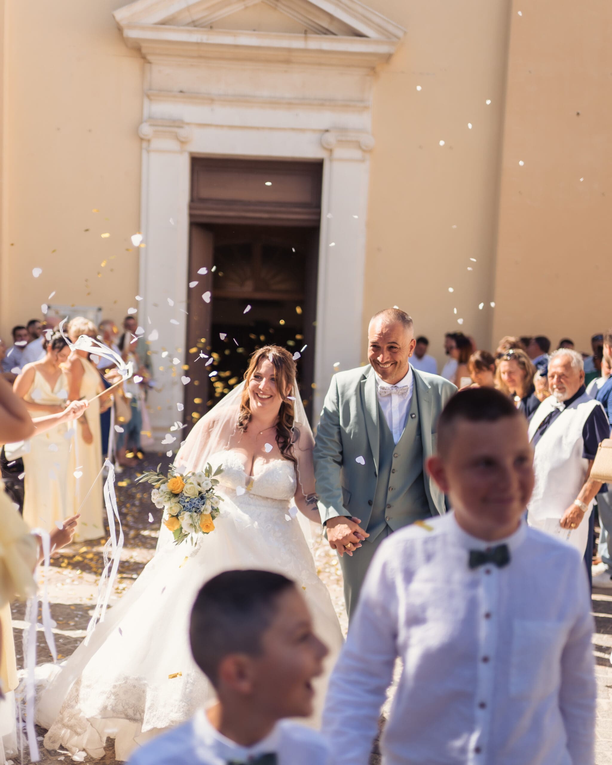 Les mariés sortent de l’église tandis que les invités les couvrent de confettis, un bouquet à la main, des sourires illuminant tous les visages.