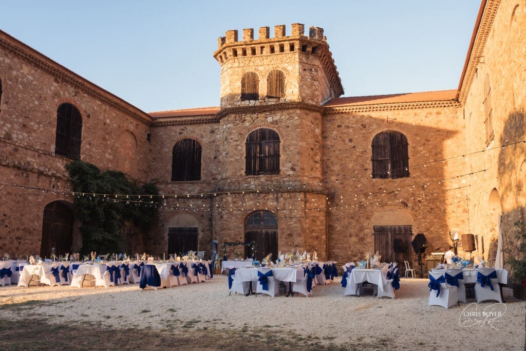 Vue du domaine en pierre avec tables de réception dressées en nappes blanches et bleu marine, au coucher du soleil.